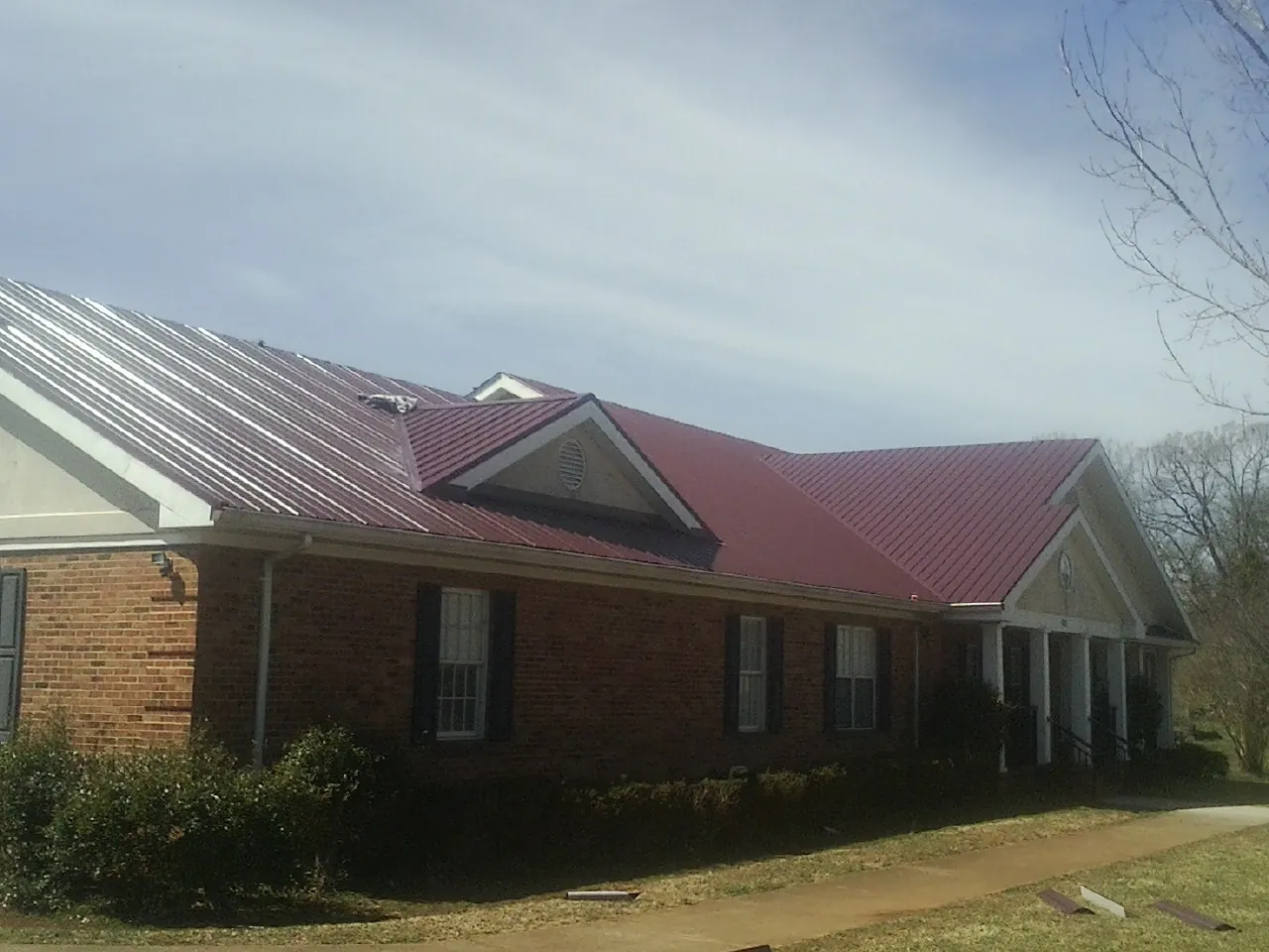 Red metal roof with gabled entries on a long brick building, from a Hail Damage Roof Repair job in Roanoke Rapids