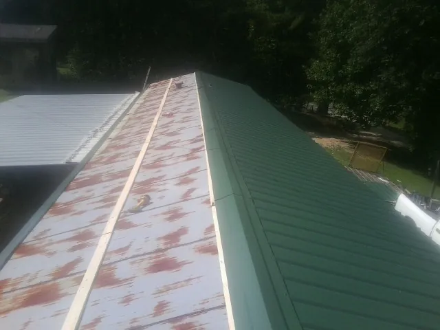 Old rusted panels beside newly installed green metal roofing — Wind Damage Roof Repair by Roofing Brothers in Roanoke Rapids
