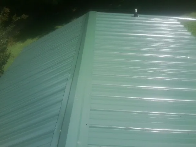 New green metal panels meeting at the ridge of a roof — Flat Roof Repair work by our crew in Roanoke Rapids