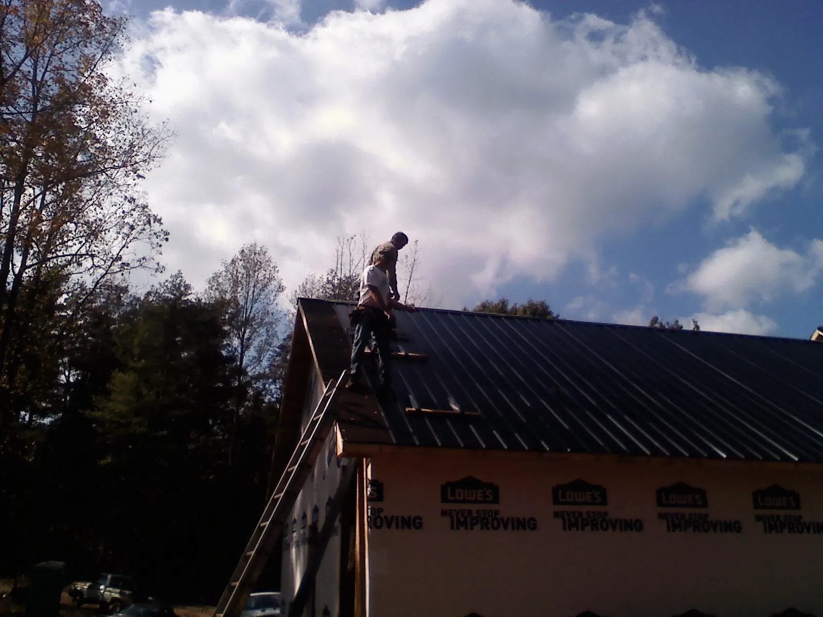 Roofer fastening dark metal panels high against a cloudy sky, from a Roof Inspection job in Roanoke Rapids