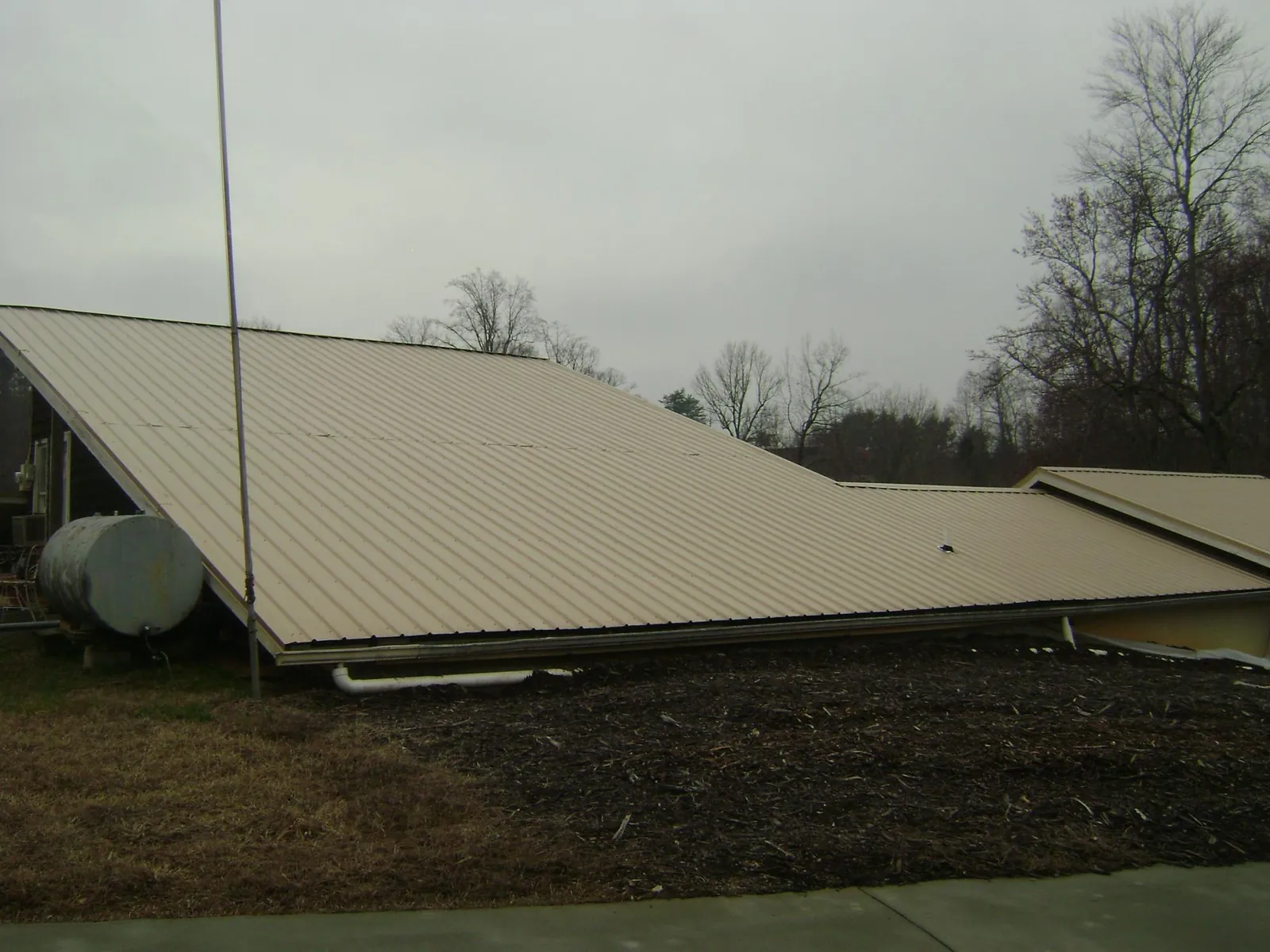 Wide tan metal roof plane seen from the ground beside a propane tank in Roanoke Rapids